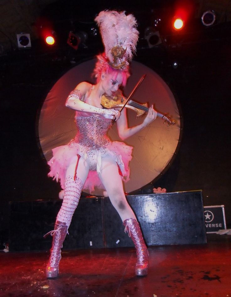 a woman in pink and white outfit holding a violin on stage with lights behind her