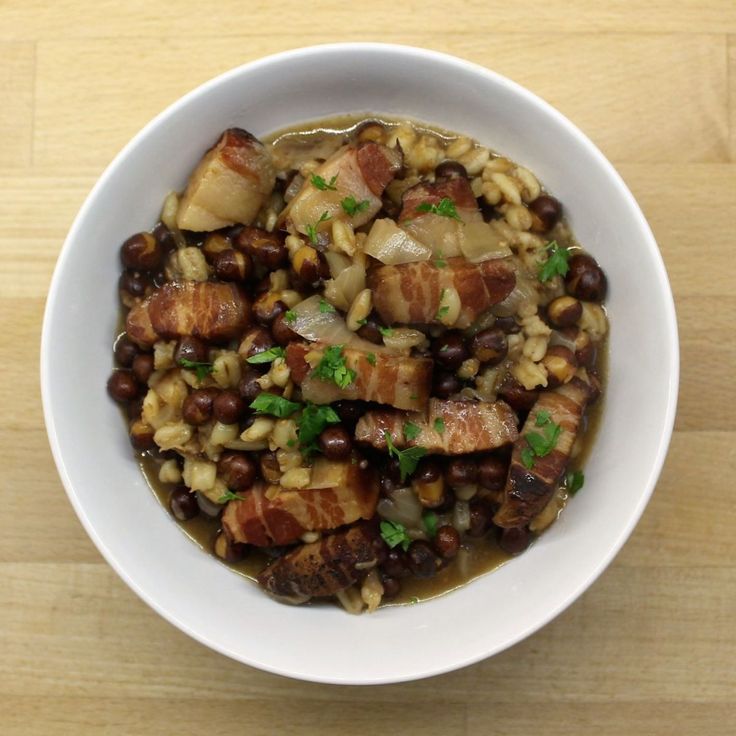 a white bowl filled with beans and meat on top of a wooden table next to a spoon