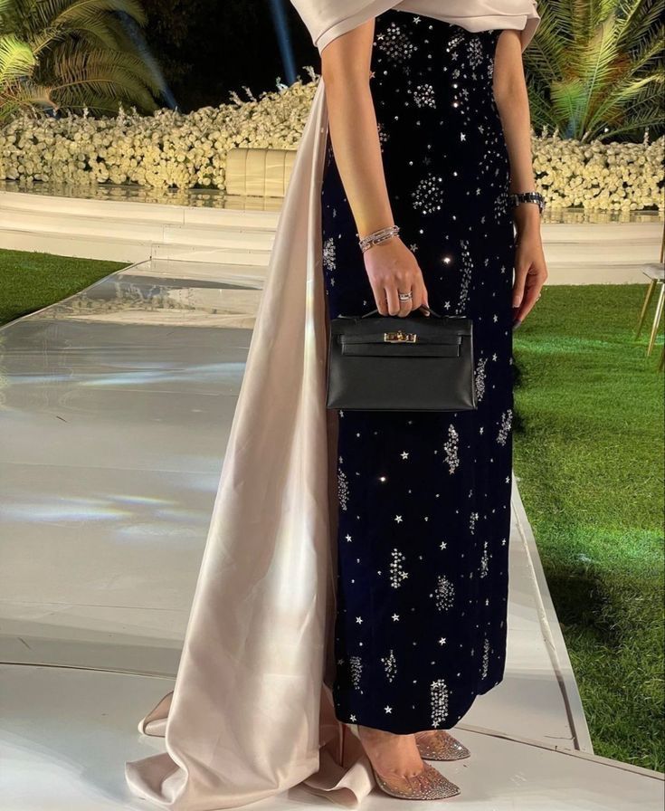 a woman standing on a runway wearing a dress and carrying a black handbag in her left hand