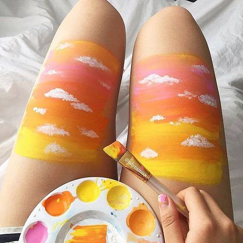 someone is painting on their legs with orange and yellow paint while holding a white plate