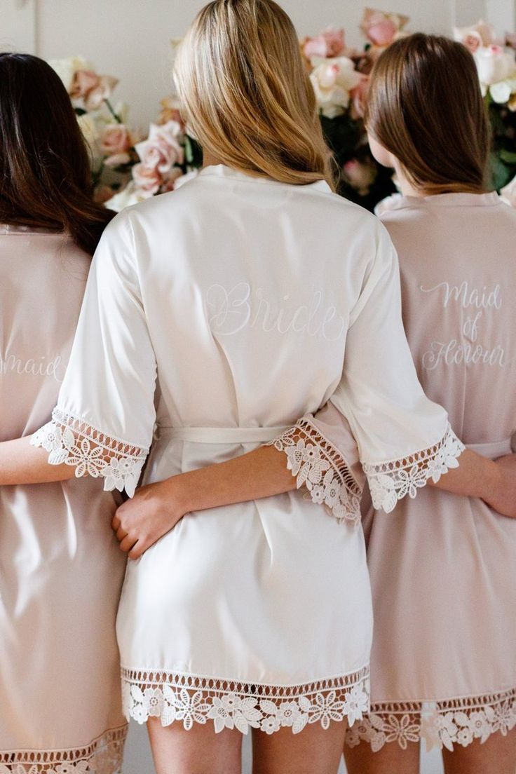 three bridesmaids in pink robes with white lace trims and name written on them