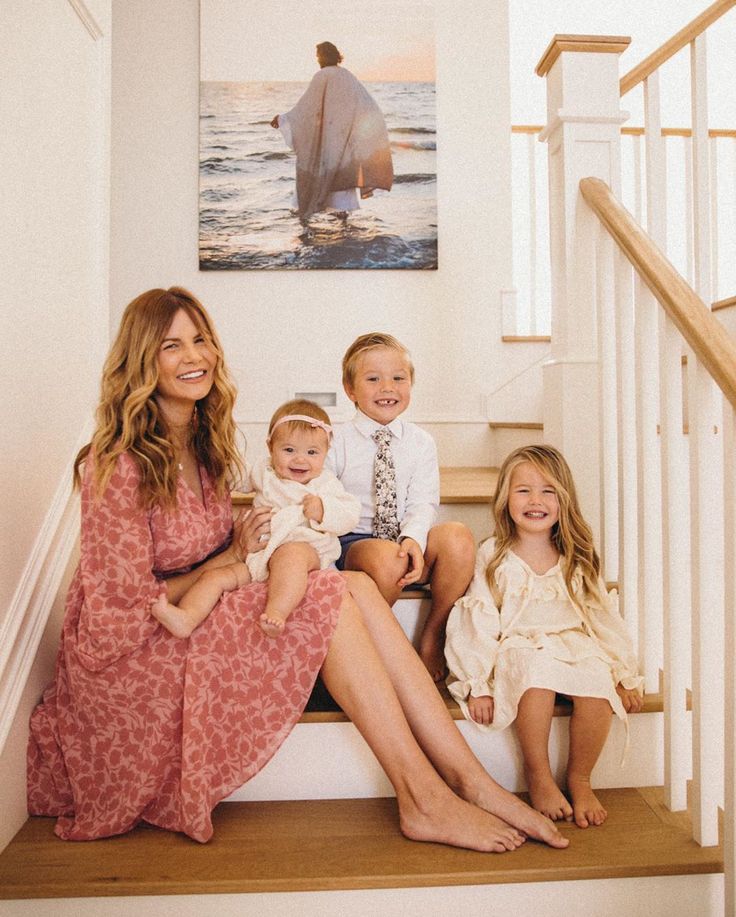 a woman and two children sitting on the stairs in front of a staircase with an art work above them