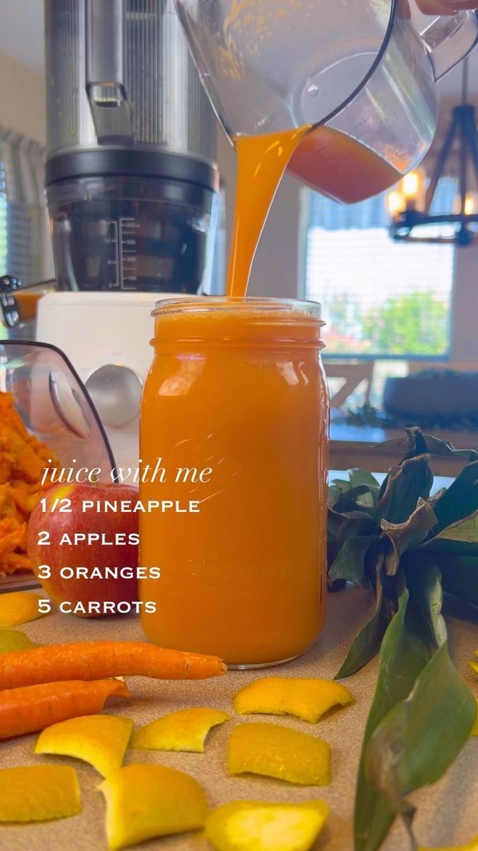 a person pouring orange juice into a jar next to sliced carrots and other vegetables