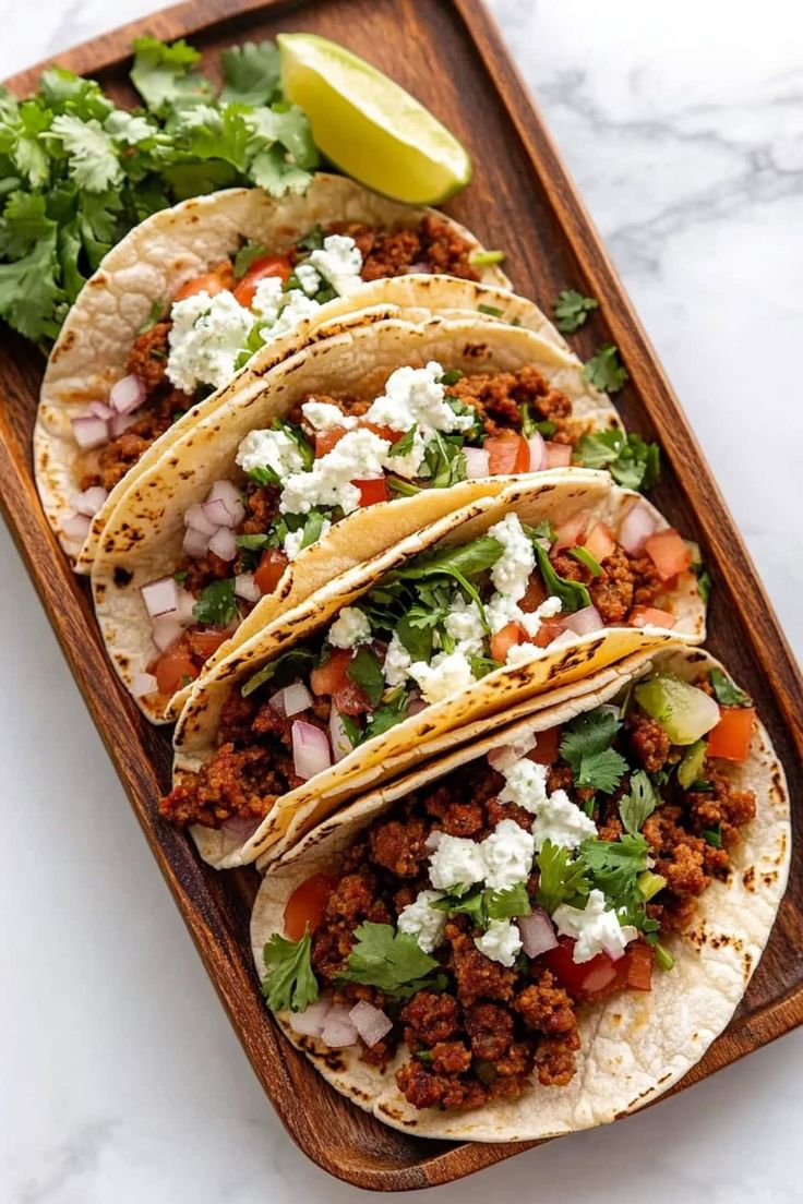 three tacos with meat and vegetables on a wooden tray