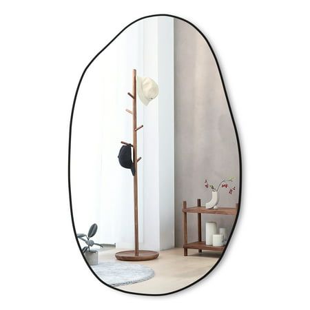 an oval mirror with a coat rack and hat on it in front of a white wall