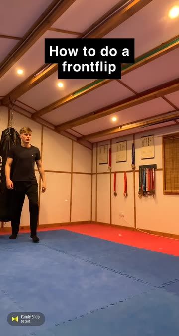 the man is practicing his martial moves in the room with blue mats and red flooring