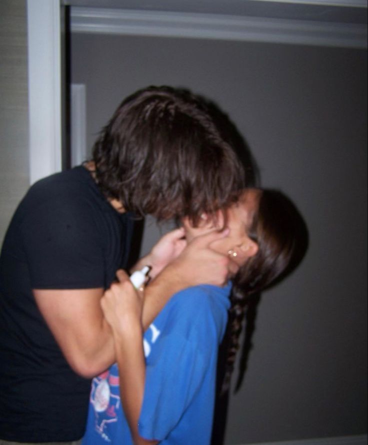 two people hugging each other in front of a door and one person wearing a black t - shirt