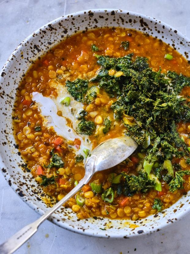 a white bowl filled with soup and broccoli on top of a table next to a spoon