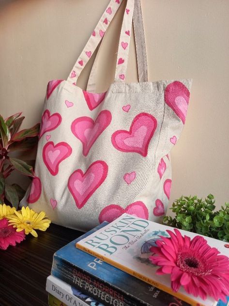 a white bag with pink hearts on it next to flowers and books