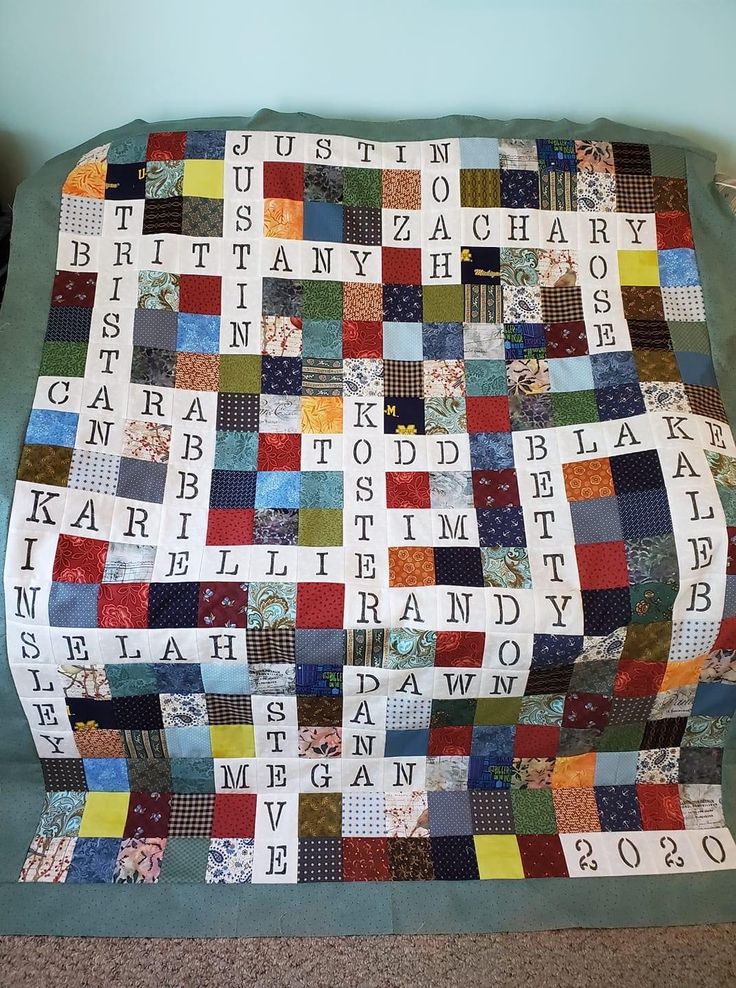 a quilted blanket with letters and numbers on it sitting on the floor in front of a blue wall