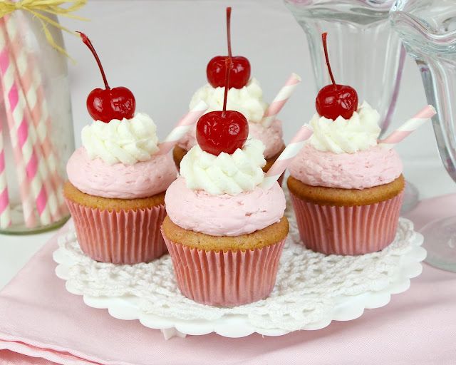 three cupcakes with cherries and white frosting on a pink doily