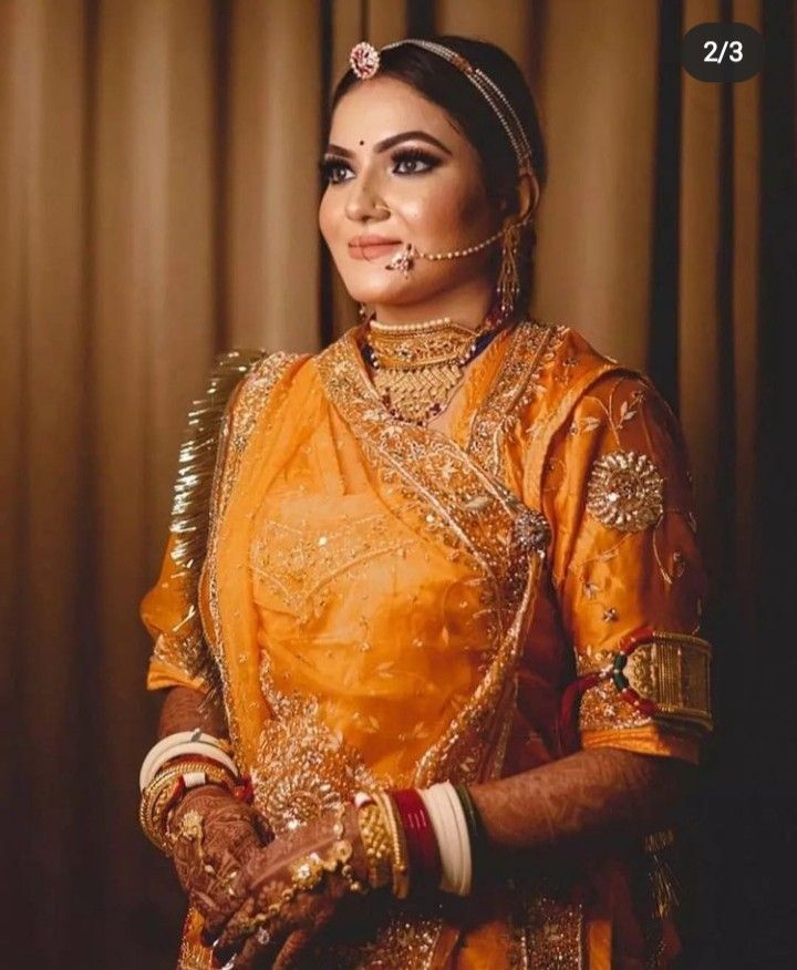 a woman in an orange and gold bridal outfit with her hands on her hips