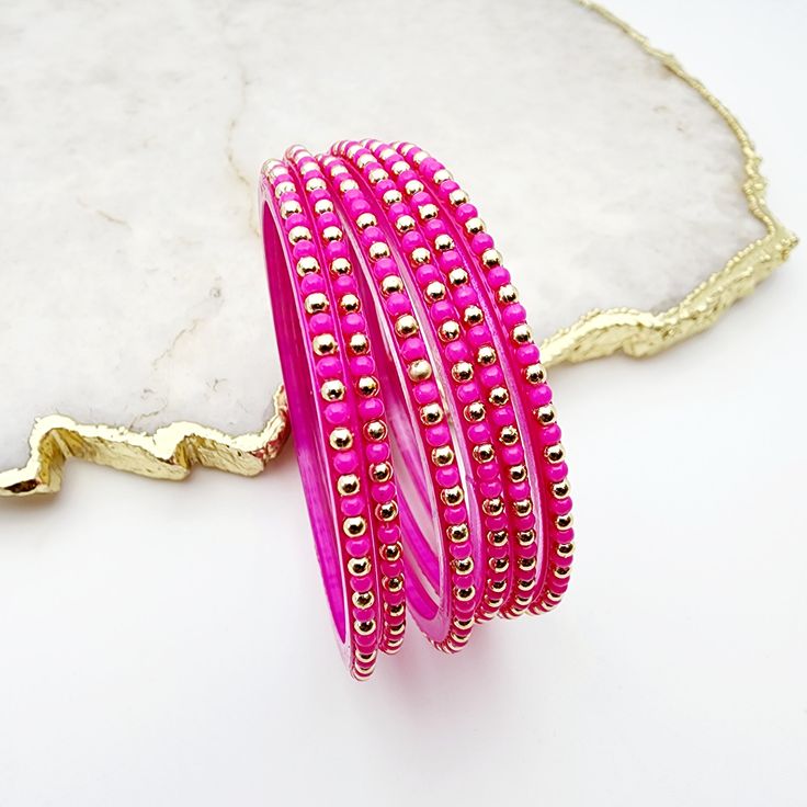 Lori Glass Bangles feature a vibrant fuschia hue accented with muted gold, adding a touch of elegance and pop of color to any outfit. Made of high-quality glass, these bangles are a must-have accessory for any fashion-forward individual. Elevate your style with Lori Glass Bangles. *Sold as a six-piece set.*To prevent any potential damage, please put on each glass bangle individually. For a snug fit, we suggest sizing up from your usual bangle size. Trendy Pink Beaded Bracelets For Party, Trendy Gold Wrap Bracelet, Gold Wrap Bracelet Fashion Accessory, Trendy Adjustable Wrap Bracelet For Party, Trendy Multicolor Party Bangle, Party Wrap Bangle Bracelet, Pink Gold Bangle Jewelry For Party, Gold Wrap Bracelet For Parties, Trendy Gold Festive Jewelry