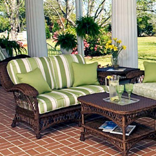 an outdoor living room with wicker furniture and green striped pillows on the couches