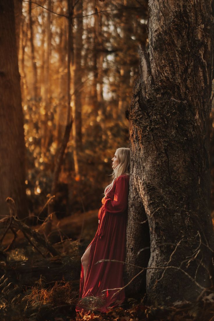 a woman in a red dress is standing next to a tree and looking up at the sky