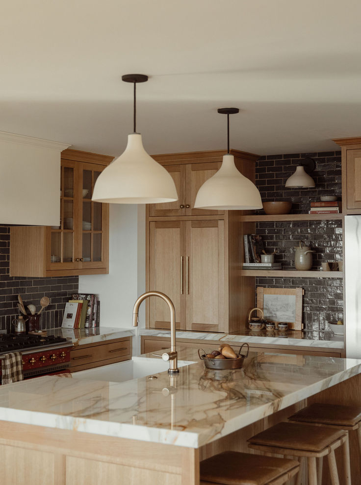 a kitchen with wooden cabinets and white marble counter tops, two pendant lights over the island