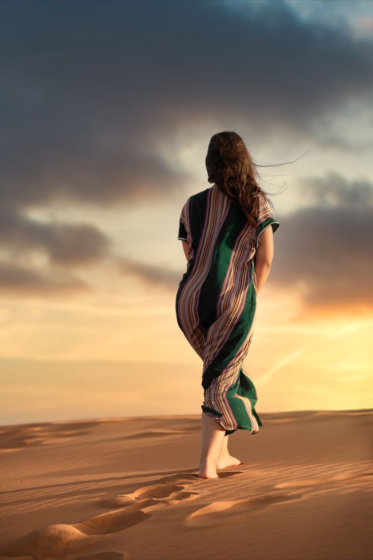 a woman standing in the desert at sunset