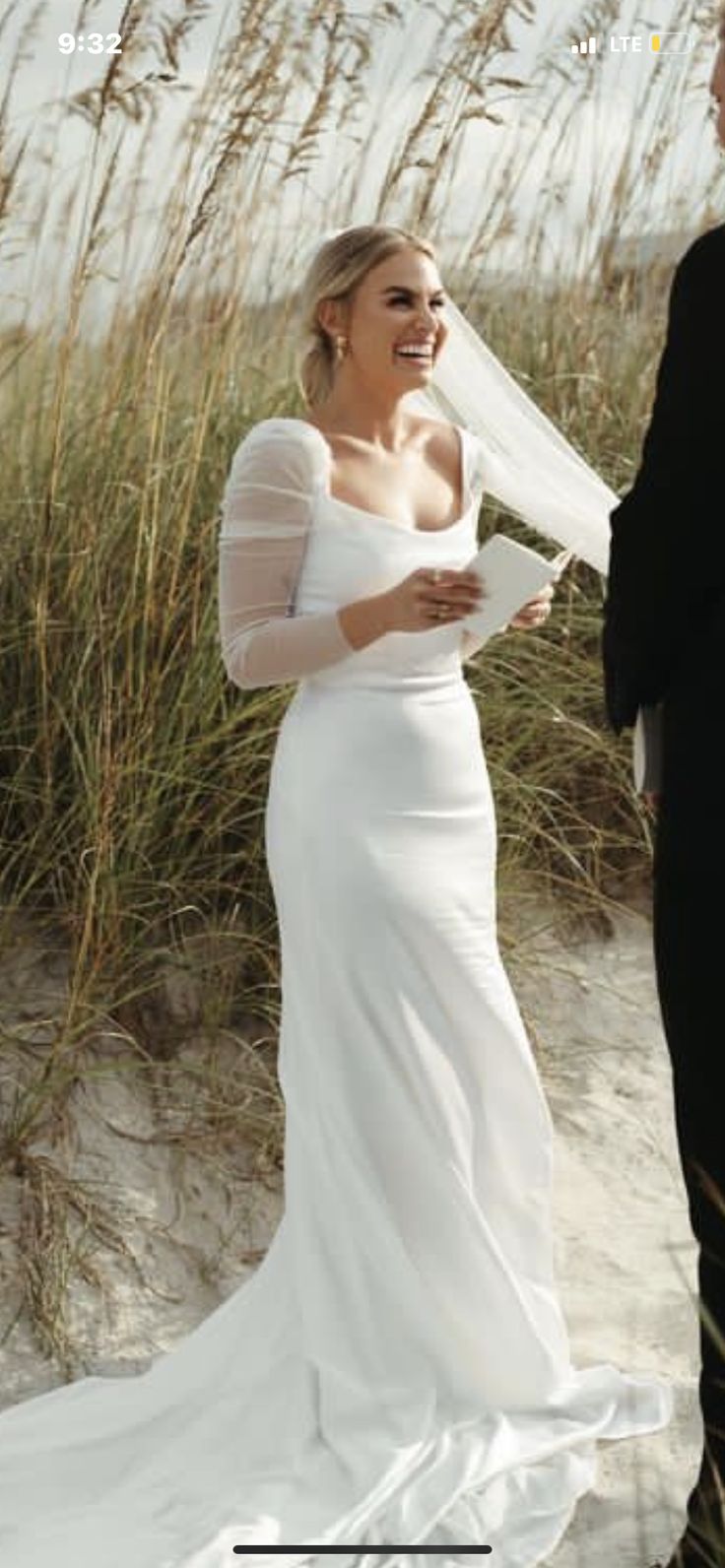 a man and woman standing next to each other on top of a sandy beach near tall grass