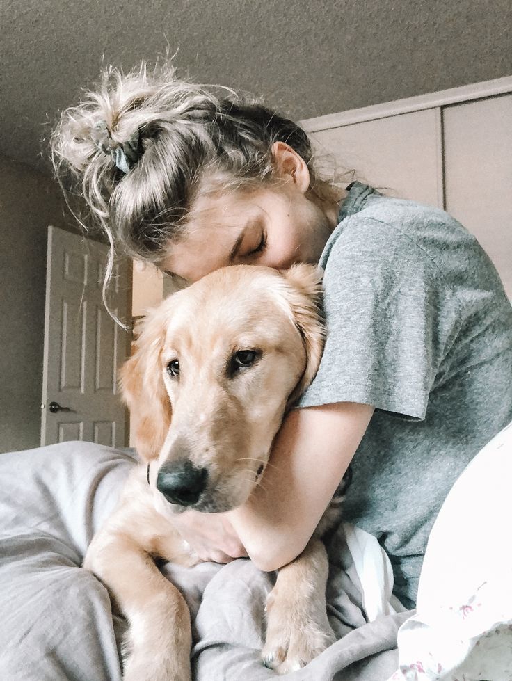 a girl hugging her dog on top of a bed in a room with gray walls