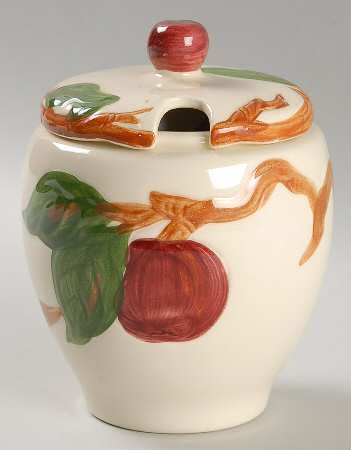 a ceramic jar with fruit painted on the side and leaves around it, sitting on a white surface