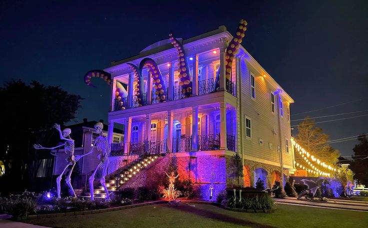 a large house decorated for halloween with lights and decorations on the front porch, along with statues