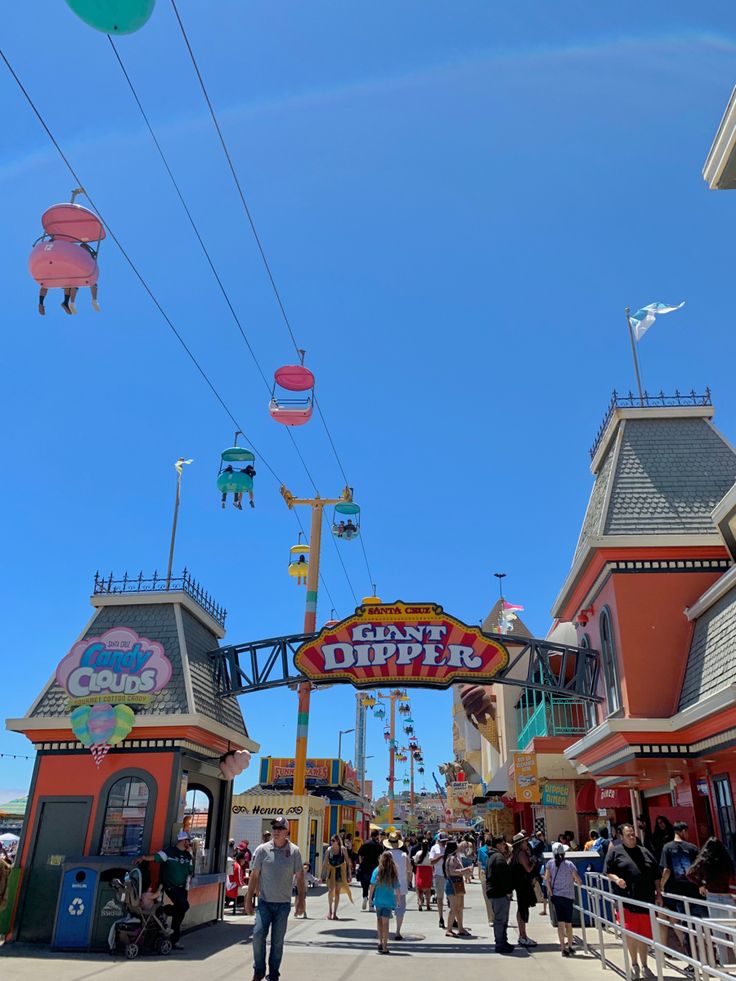 the entrance to an amusement park with lots of people walking around and riding on roller coasters