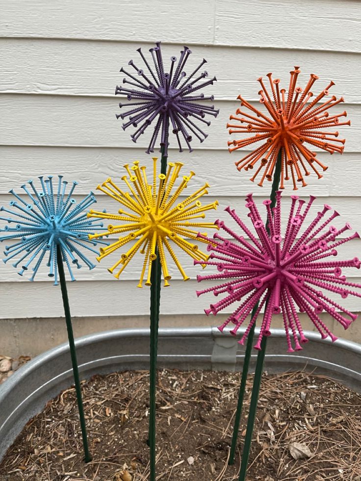 three brightly colored paper flowers in a metal planter on the side of a house