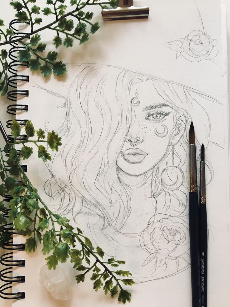 a pencil drawing of a woman's face surrounded by greenery and flowers on top of a notebook