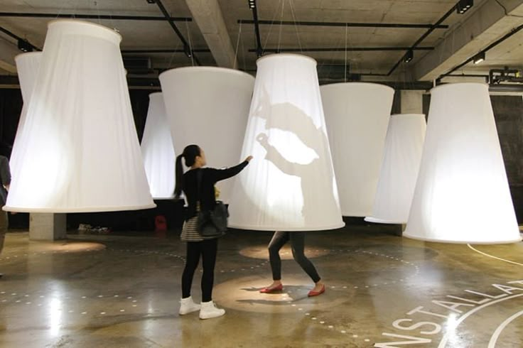 two women standing in front of giant white lamps with their hands on the lightshades