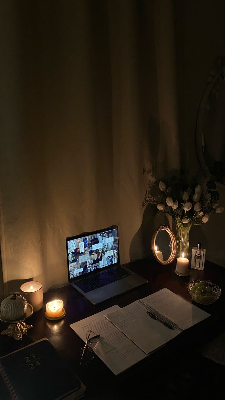 a laptop computer sitting on top of a wooden desk next to a vase with flowers