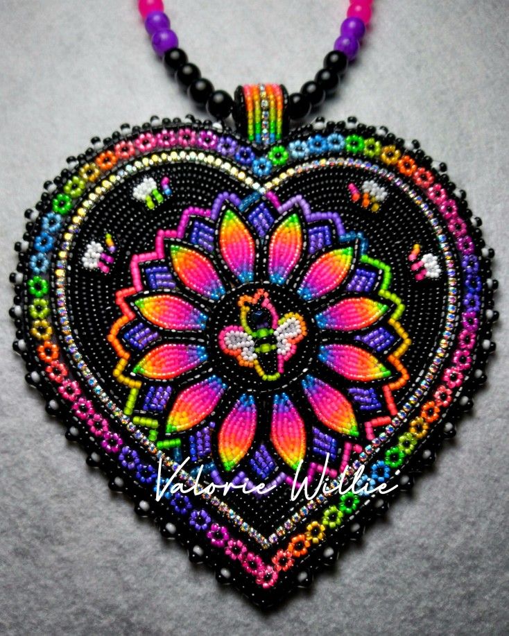 a heart shaped beaded necklace with colorful beads and flowers on the front, sitting on a white surface