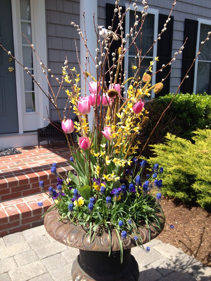 a vase filled with lots of flowers sitting on top of a brick walkway next to a house