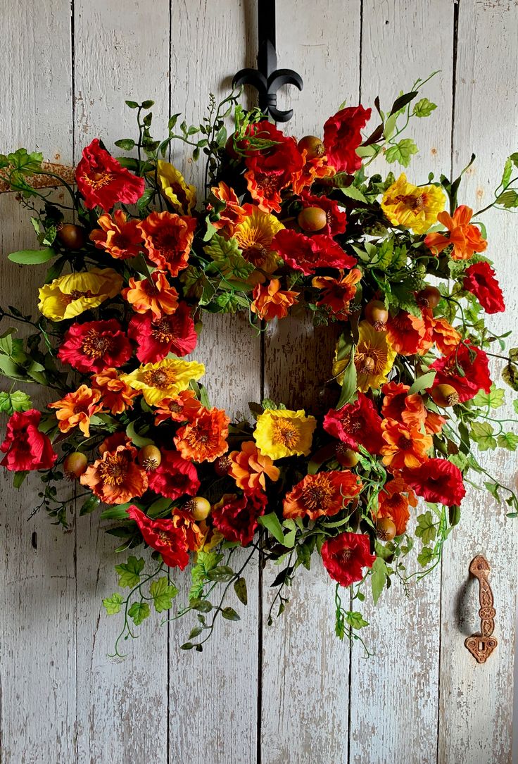 a wreath hanging on the side of a white wooden wall with flowers in front of it