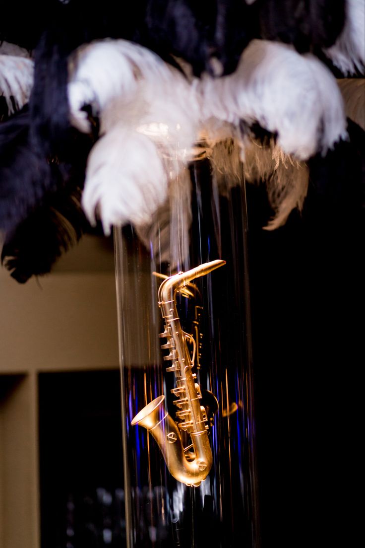 a close up of a glass vase with a saxophone on it's side and feathers hanging from the ceiling