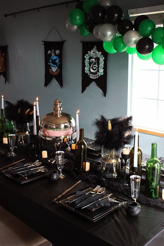 a table set up for a harry potter party with green and black balloons, silverware, wine bottles, candles and plates