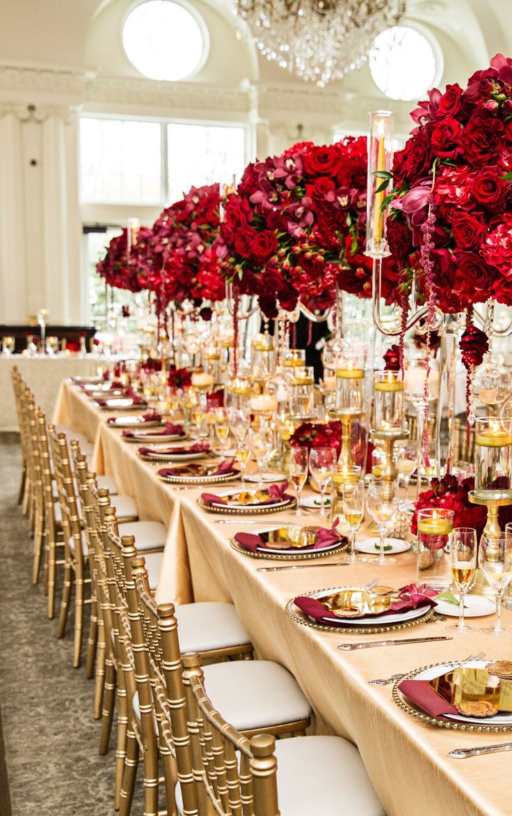 a long table is set with red flowers and gold place settings