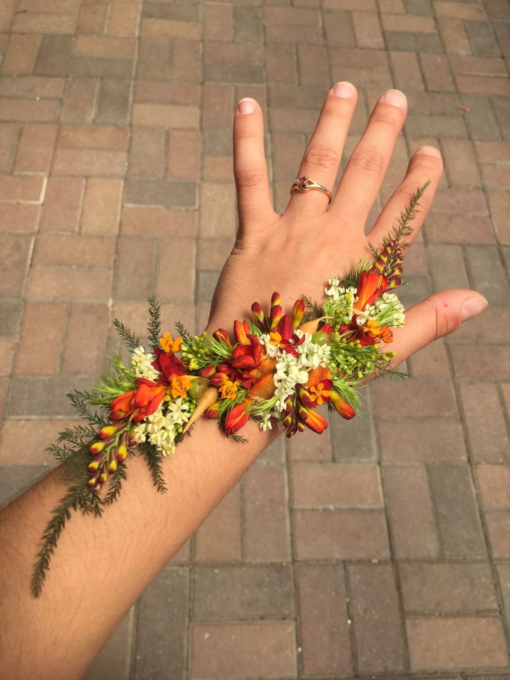 a person's hand with flowers and greenery on it, against a brick background