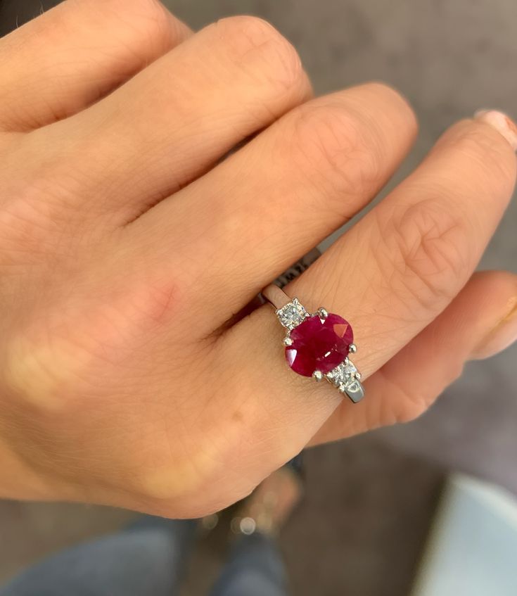 a woman's hand holding a ring with an oval shaped ruby and diamond center