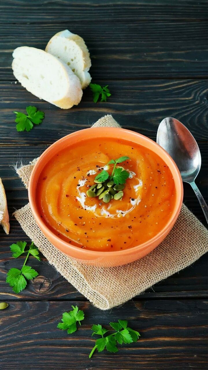 a bowl of carrot soup with bread and parsley on the side next to it