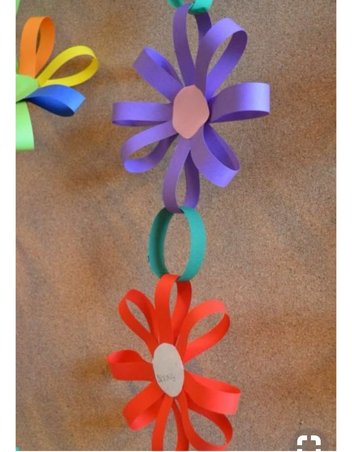 colorful paper flowers hanging from a string on a brown cloth covered floor, with one flower in the center