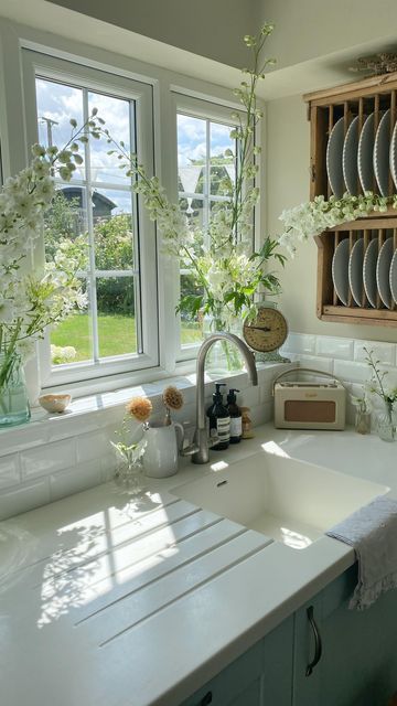 a kitchen with white counter tops and dishes on the rack in front of two windows