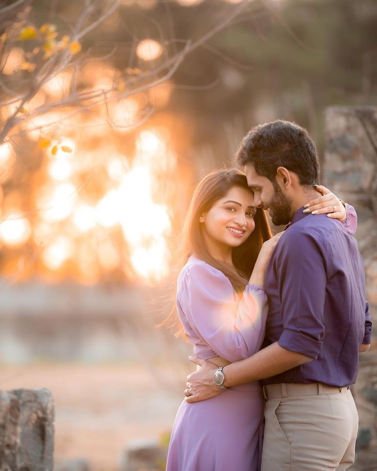 a man and woman standing next to each other in front of a tree at sunset