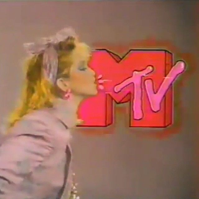 a woman with blonde hair and pink lipstick standing in front of a tv sign that says mmm