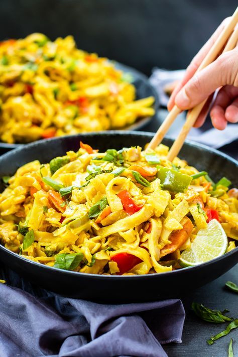 someone is holding chopsticks over a bowl of noodles with vegetables and sauce on the side