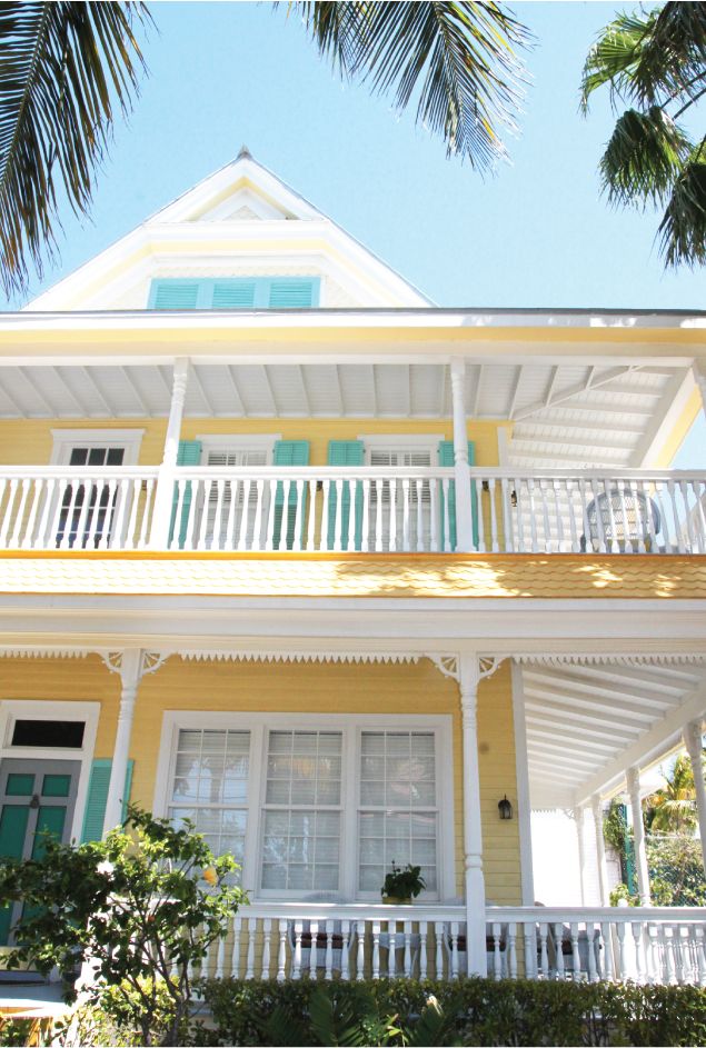 a yellow house with white balconies and green shutters on the second story