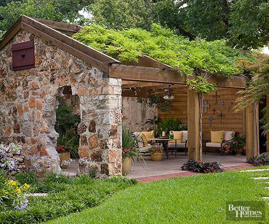 a stone building with a green roof and plants growing on it's sides, in the middle of a garden