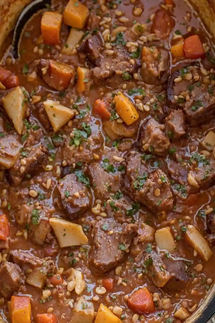 a pot full of stew with carrots, potatoes and meat in it on top of a wooden table