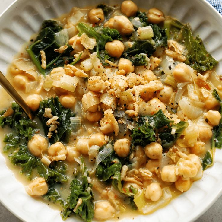 a white bowl filled with chickpeas and spinach on top of a table