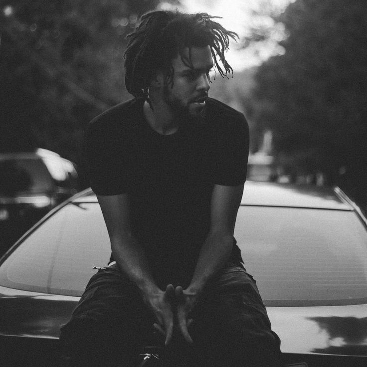 a man with dreadlocks sitting on the hood of a car