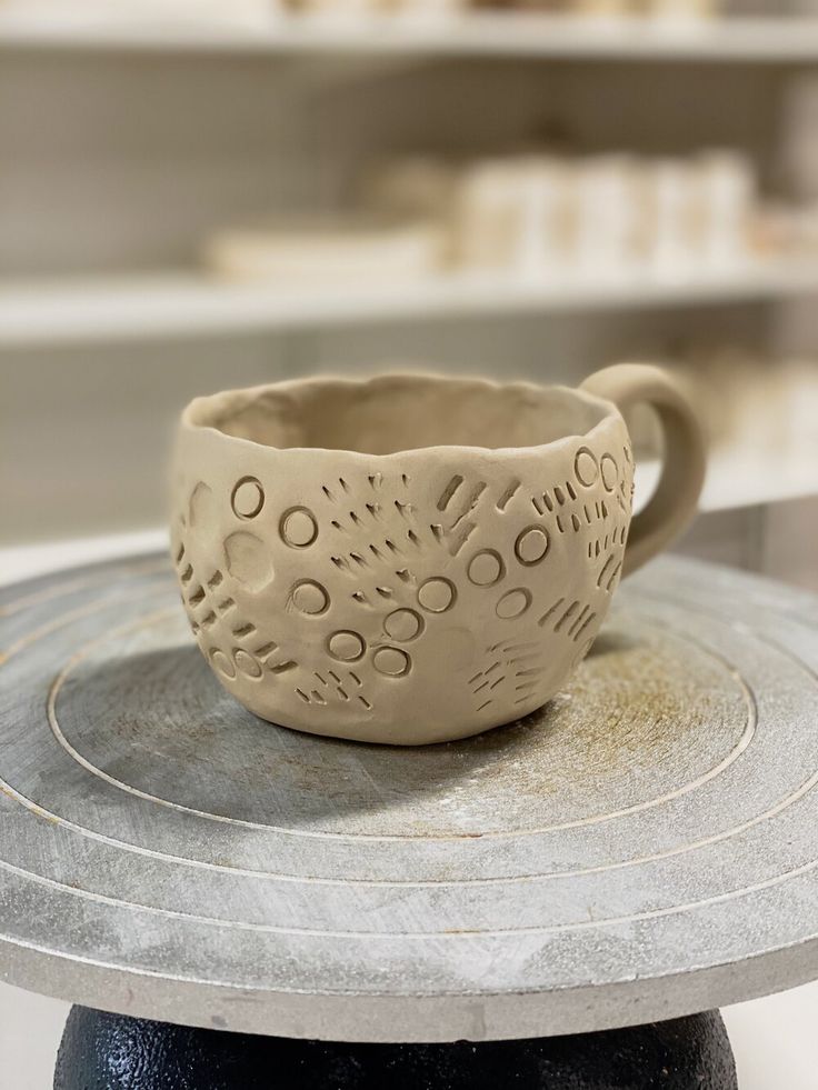 a ceramic cup sitting on top of a metal table next to a black pot with holes in it